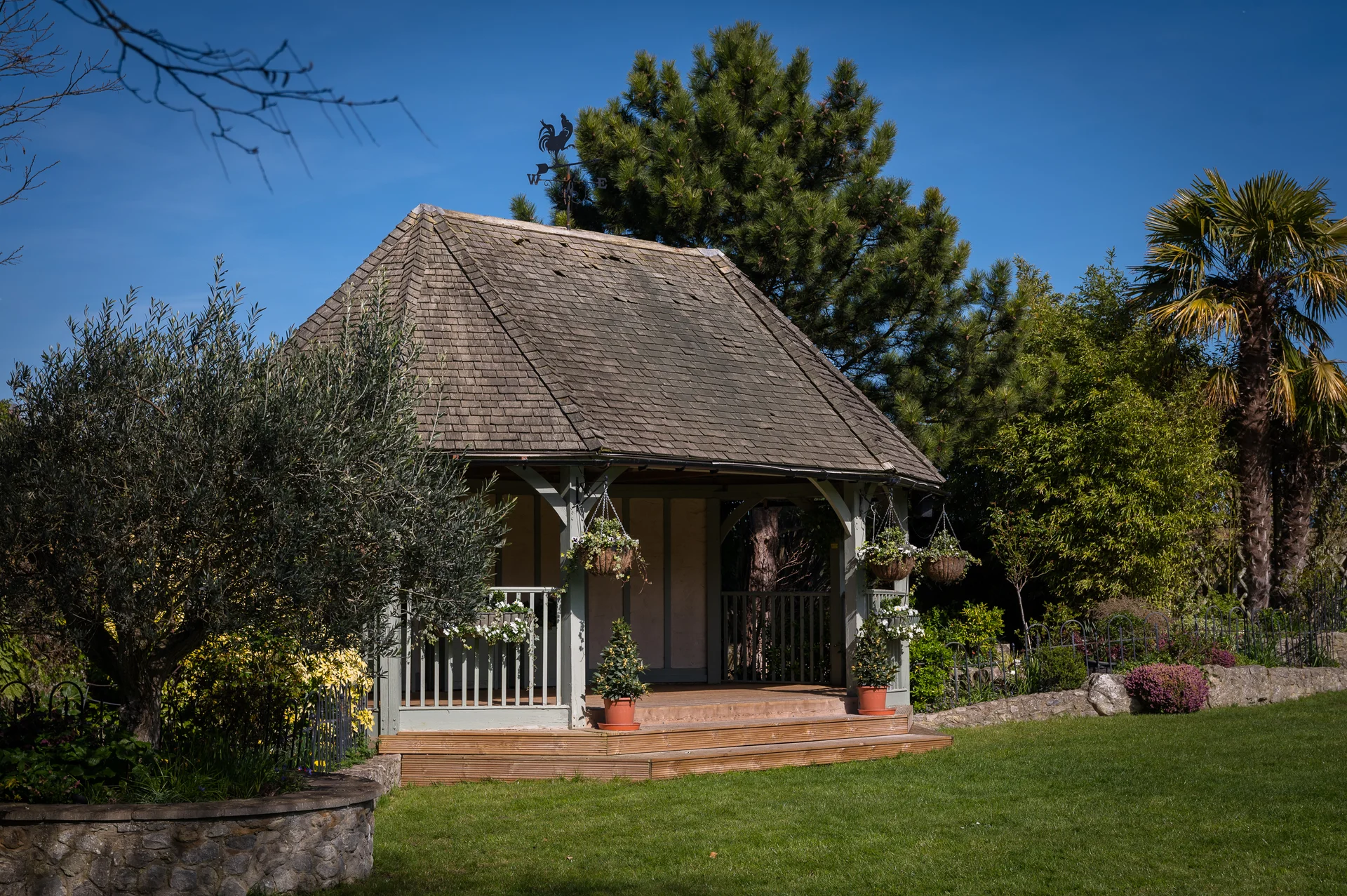 A charming wooden gazebo stands on a lush green lawn beneath a clear blue sky during a sunny wedding day.