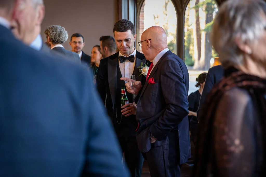 Guests mingling and chatting during a drinks reception inside a venue with large arched windows.