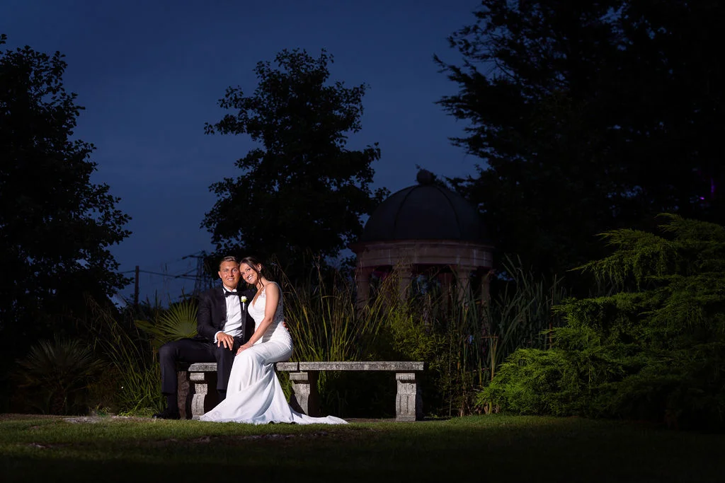 A bride and groom sitting on a bench at night.