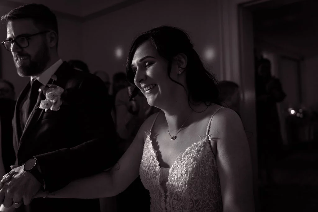 A newlywed couple laughing joyfully together during their wedding celebration, captured in a moody black and white shot with natural lighting.