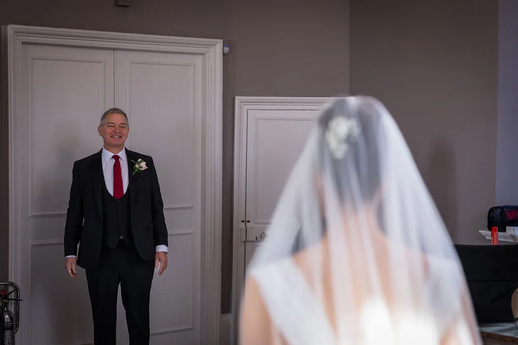 An emotional father smiles warmly as he sees his daughter in her wedding dress and veil for the first time.