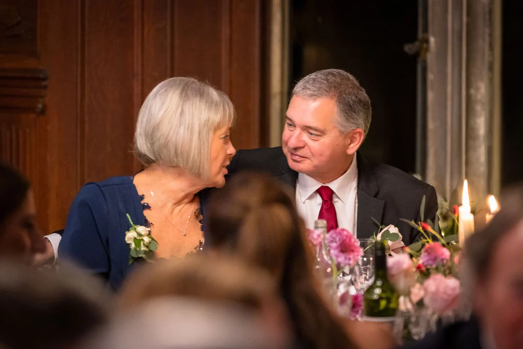 An older couple shares a tender, whispered moment together at a candlelit wedding reception table adorned with floral centerpieces.