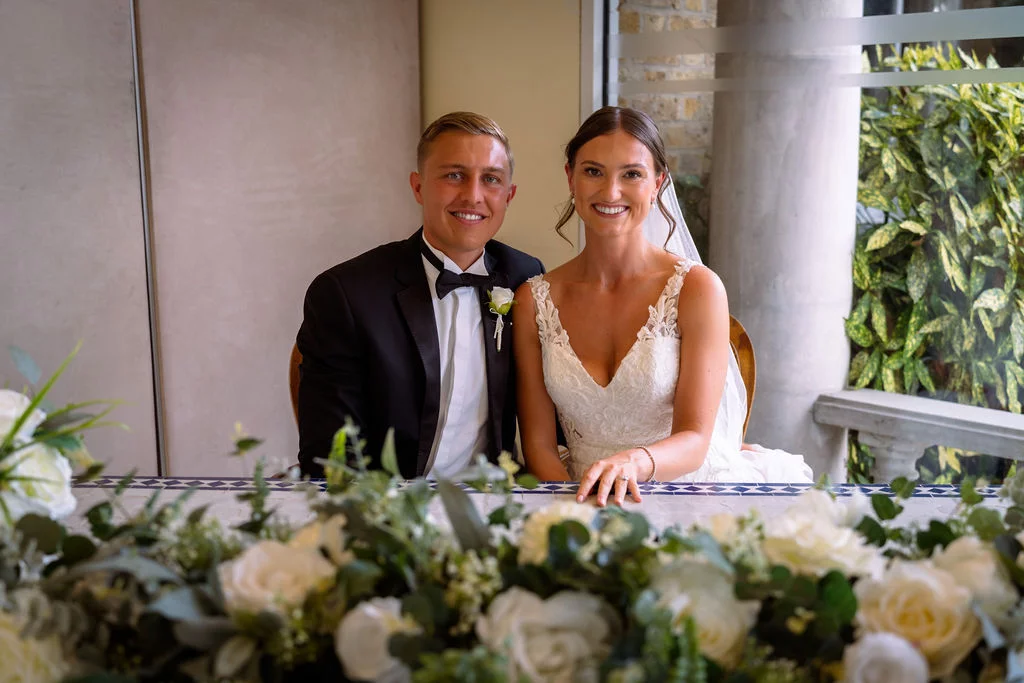 A bride and groom posing for a photo in front of a window.