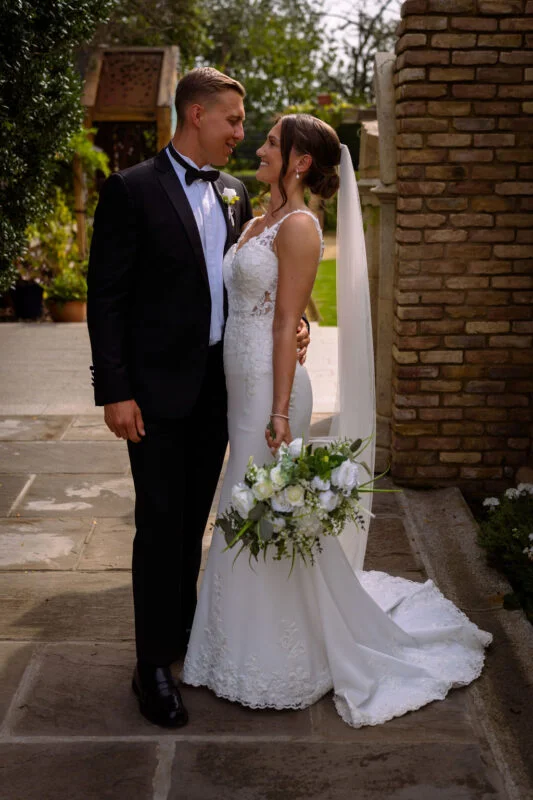 A bride and groom standing in front of a brick wall.