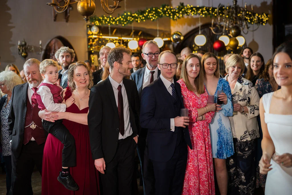 A candid group of smiling wedding guests in a warmly lit, festive venue enjoy the evening celebrations together.