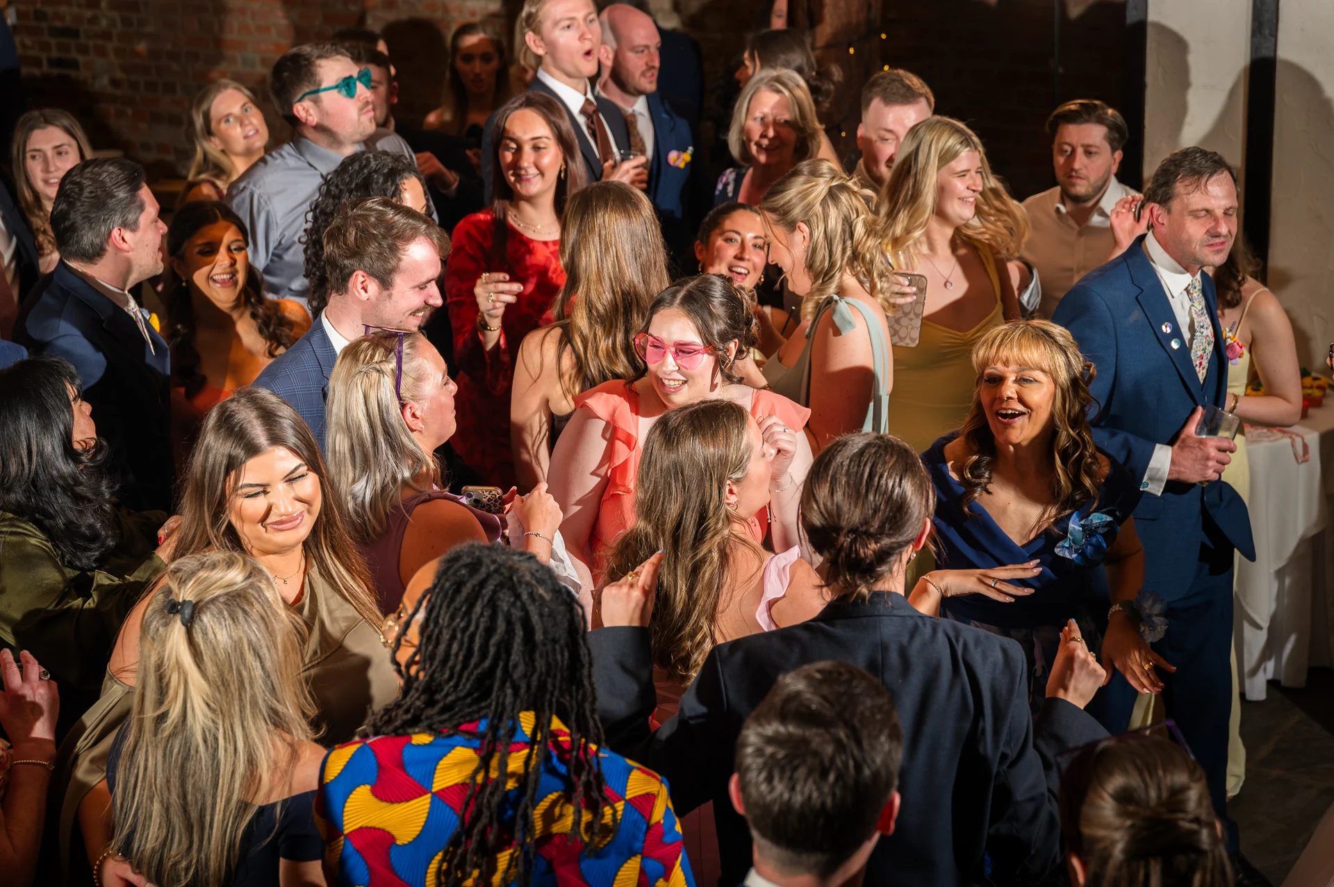A lively and crowded dance floor at an evening wedding reception where guests are laughing, socialising, and celebrating together under direct flash lighting.