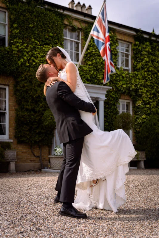 A bride and groom kissing in front of a house.