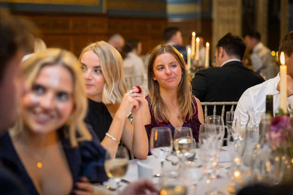 Wedding guests enjoy a candlelit wedding breakfast seated around a long banquet table in a wood-panelled room.