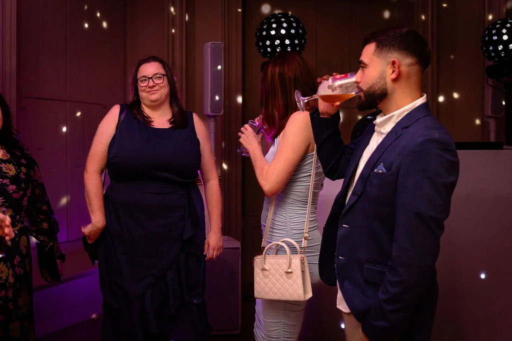Wedding guests socialising and enjoying drinks at an evening party illuminated by atmospheric pink and purple lighting.