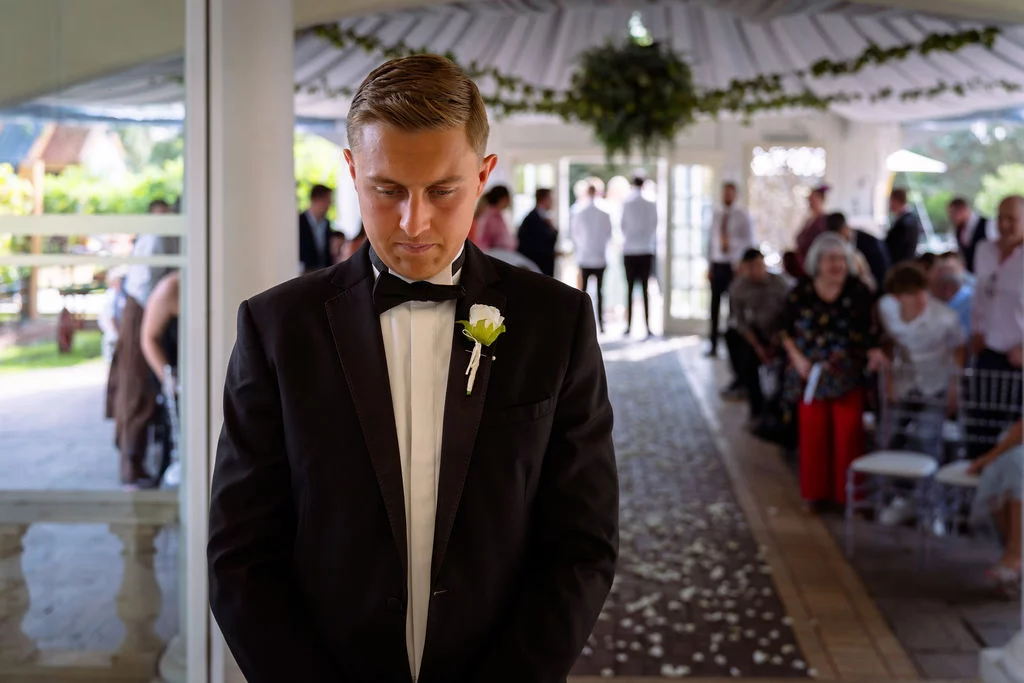 A man in a tuxedo standing in front of a wedding ceremony.