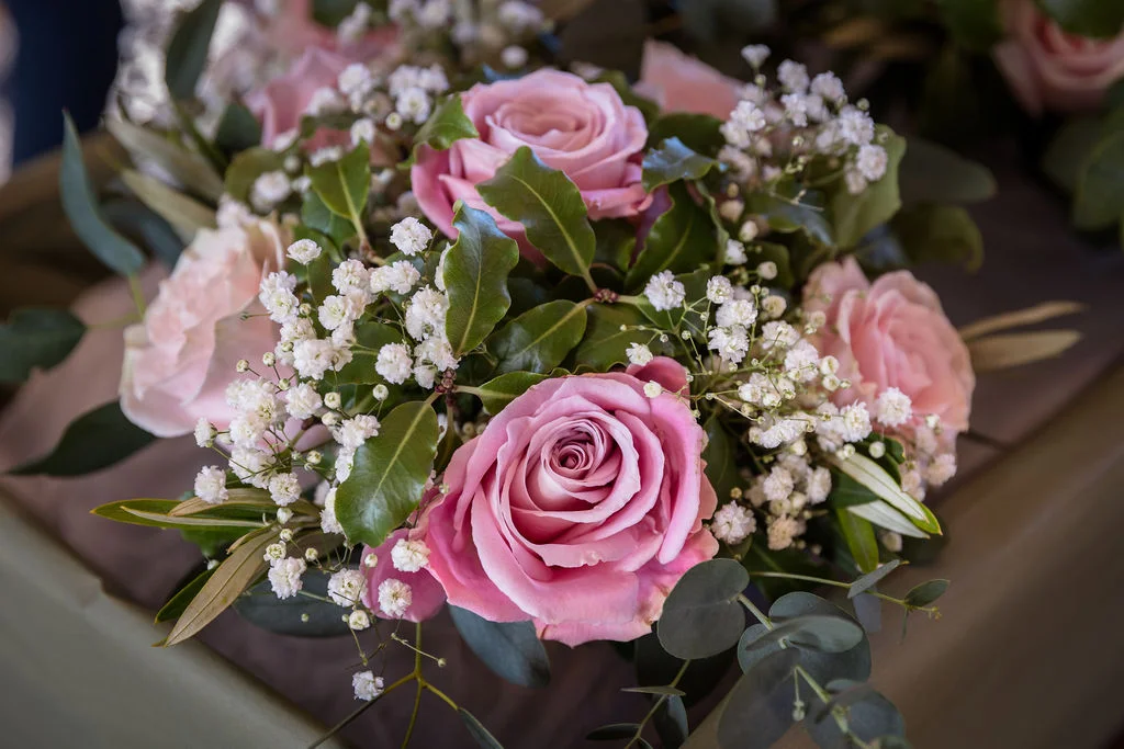 A close-up shot of a hand-tied wedding bouquet featuring soft pink roses, delicate baby's breath, and green eucalyptus foliage.