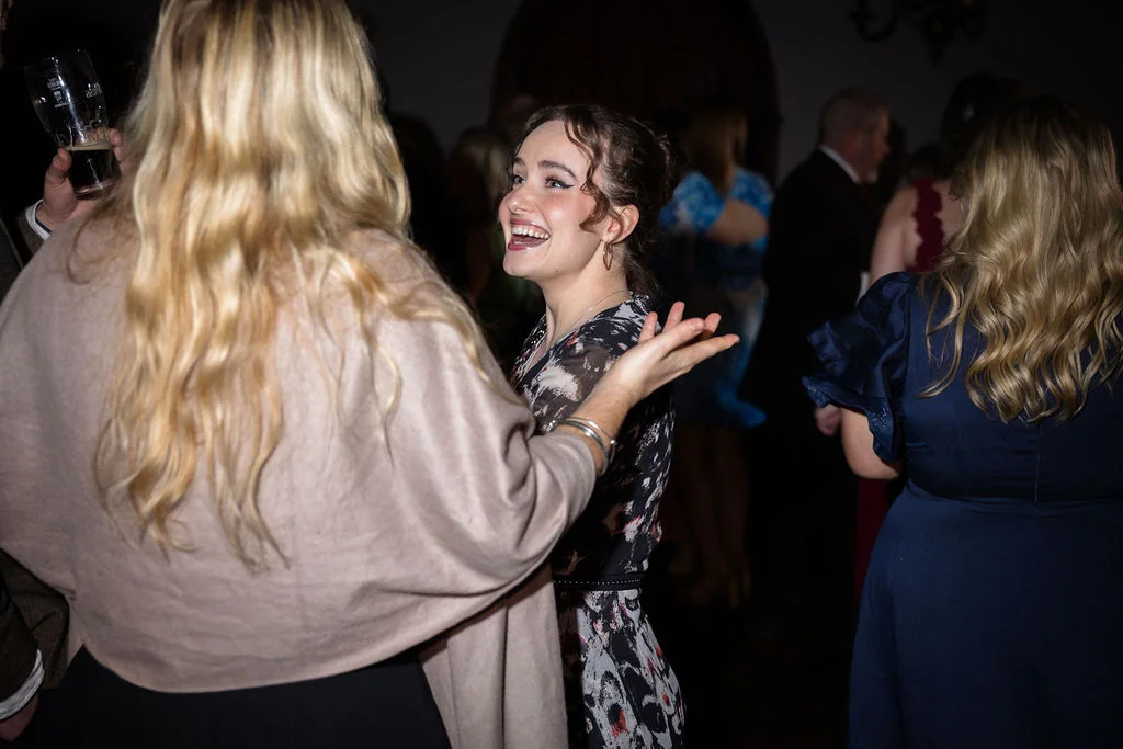 A joyful wedding guest laughs enthusiastically while chatting with friends during an evening reception illuminated by direct flash.
