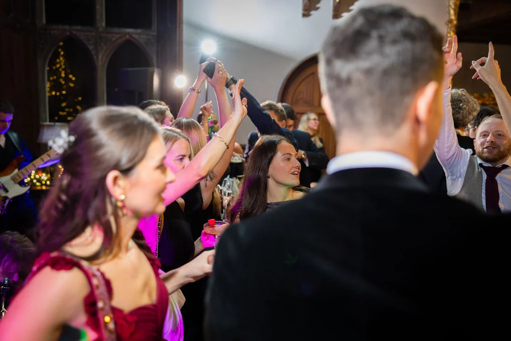 Wedding guests enjoy the lively evening reception on a crowded dance floor with a live band performing in the background.