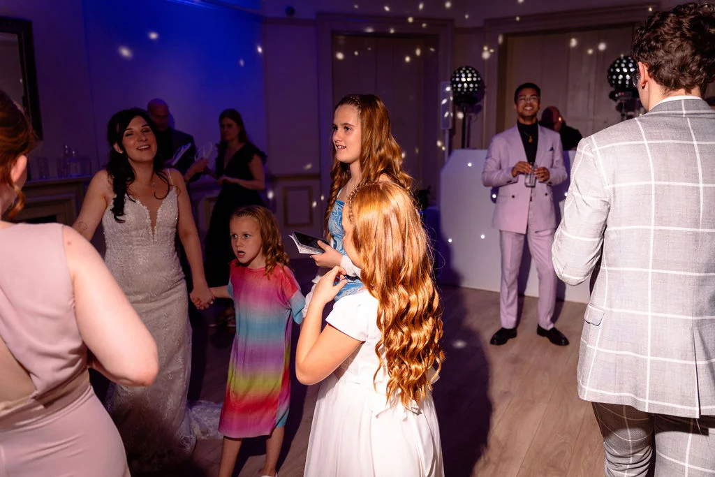Wedding guests and children enjoy dancing inside a venue illuminated by blue lighting and disco balls during the evening celebration.