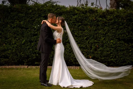 A bride and groom kissing in front of a hedge.