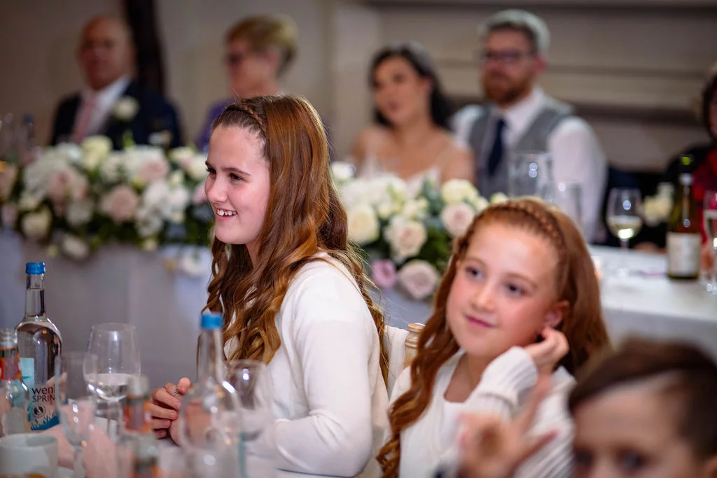 Young wedding guests smiling and enjoying themselves at a decorated reception table during the wedding breakfast.