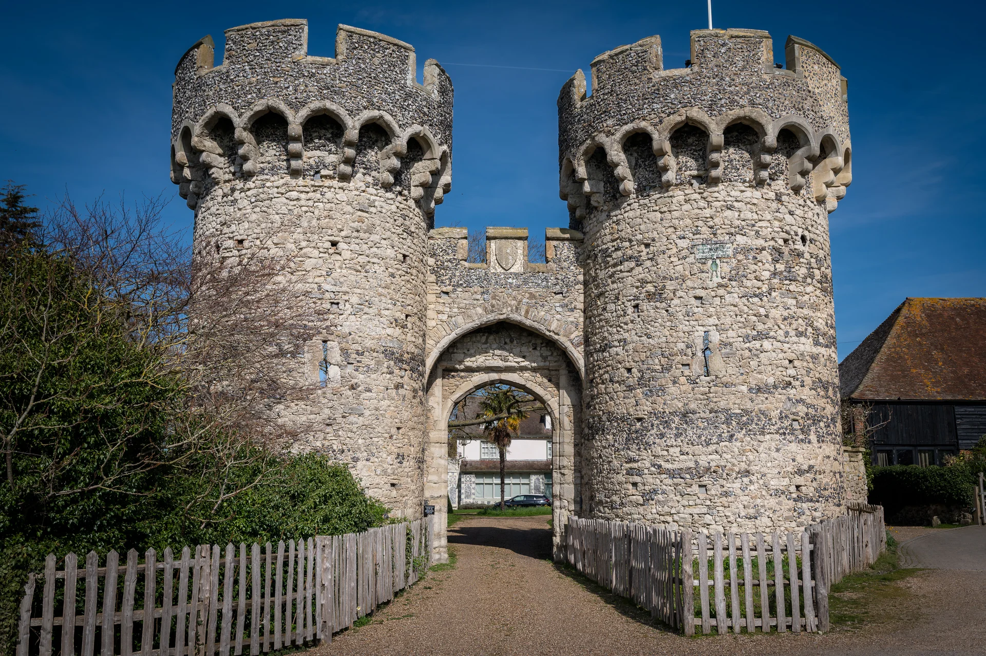 An impressive medieval stone gatehouse with twin round towers stands under a clear blue sky on a sunny day.