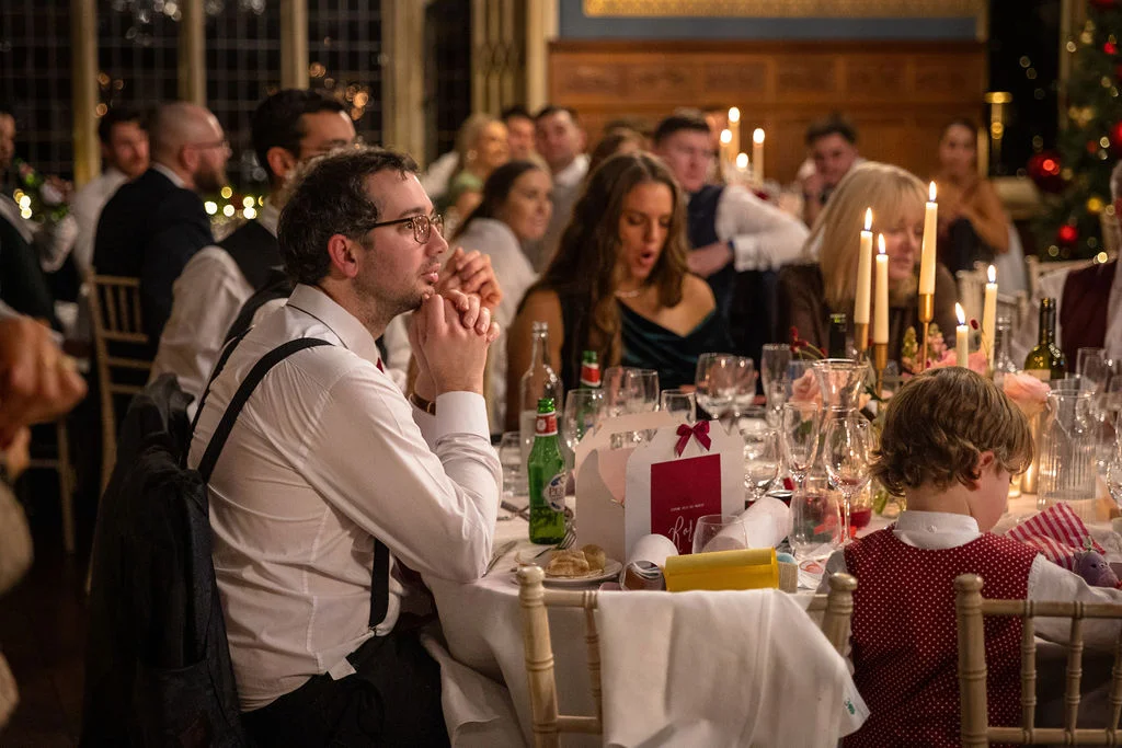 Wedding guests enjoy animated conversation and drinks during the evening wedding breakfast seated at a candlelit round table.