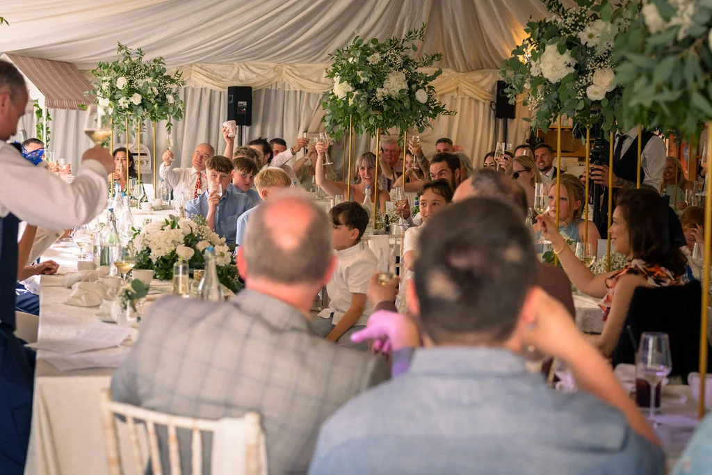 Wedding guests raise their glasses in a toast inside a elegantly draped marquee during the wedding breakfast speeches.