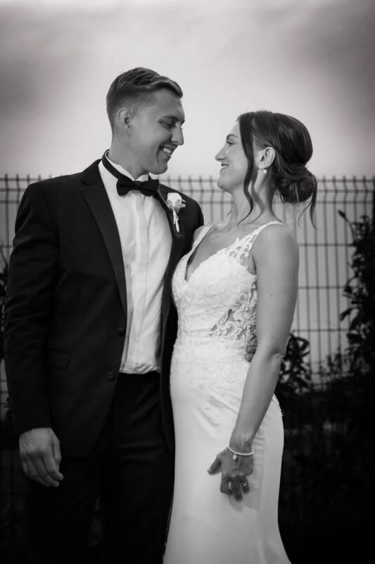 A bride and groom smiling in front of a fence.