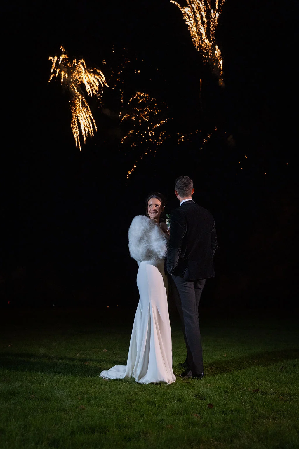 A newlywed couple watches a stunning fireworks display light up the night sky during their winter wedding reception celebration.