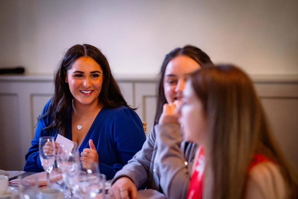 Three wedding guests laughing and chatting together at a reception table, with one woman wearing a vibrant blue dress.