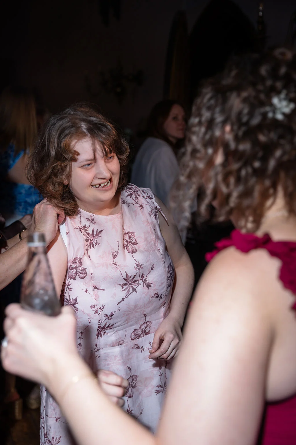 A joyful guest wearing a pink floral print dress laughs while chatting with another wedding attendee during the evening reception.