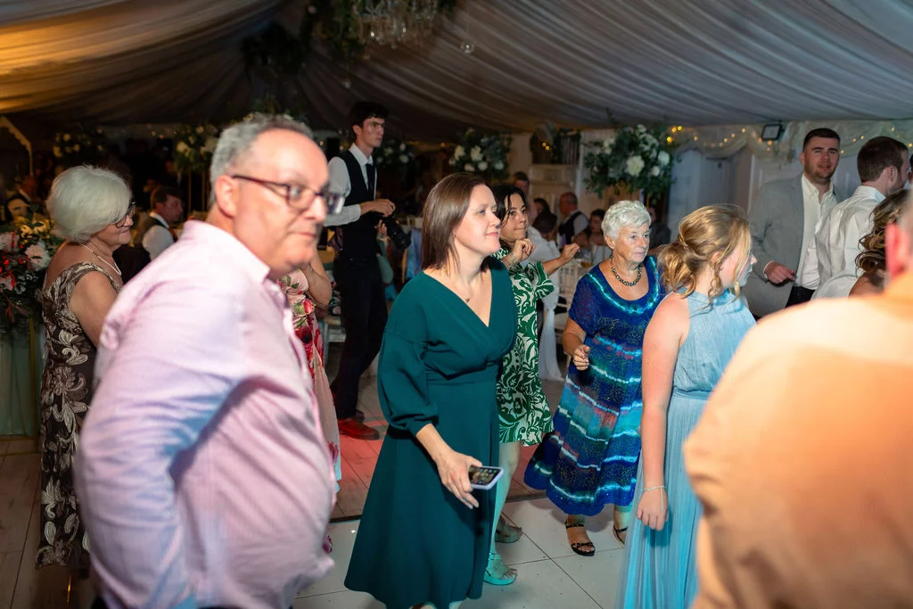 Wedding guests enjoy dancing together on the illuminated white dance floor inside a fabric-draped marquee.
