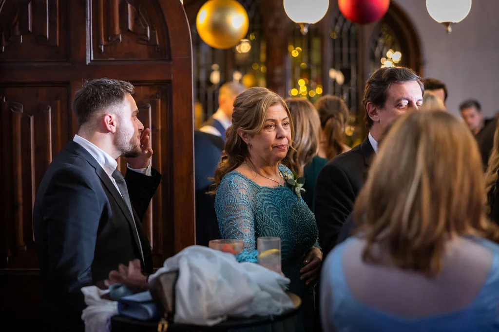 Wedding guests mingling and enjoying drinks during a reception inside a wood-panelled venue illuminated by warm overhead lighting.