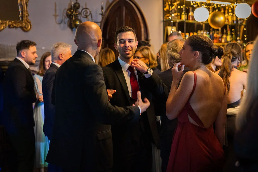 Wedding guests mingling and chatting during a lively evening reception in a bar area decorated with warm lighting.