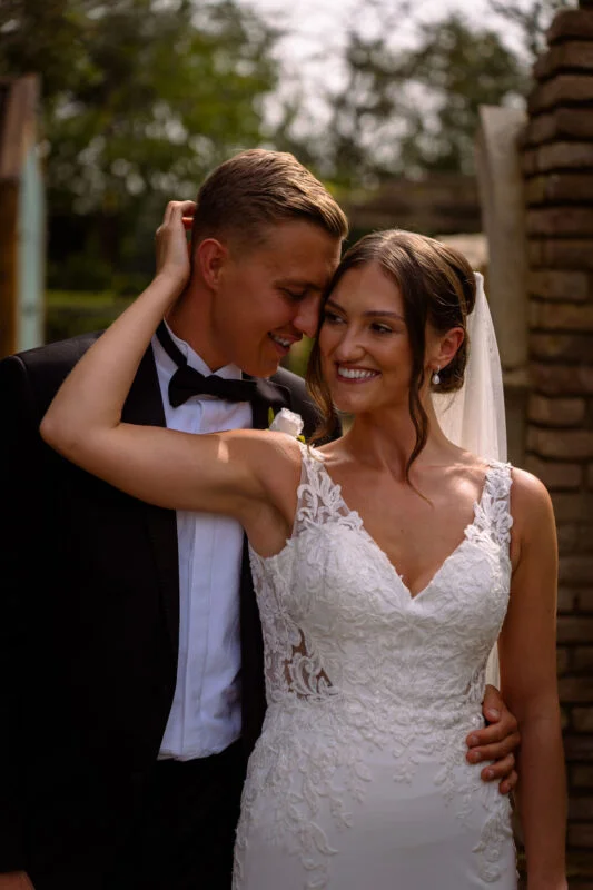 A bride and groom embracing in front of a brick wall.