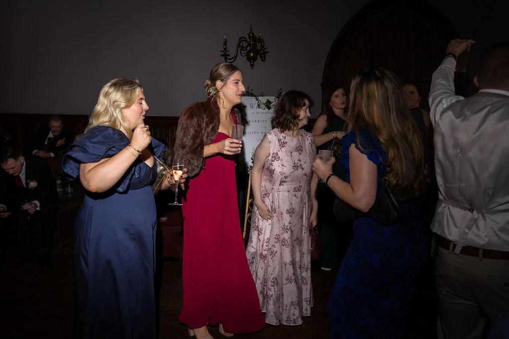 Wedding guests socialise and enjoy drinks during the evening reception inside a dimly lit venue illuminated by direct flash photography.