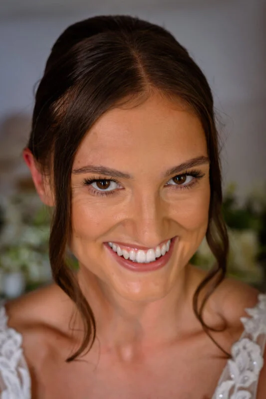 Close-up portrait of a smiling bride with dark hair framing her face and wearing a lace wedding dress.