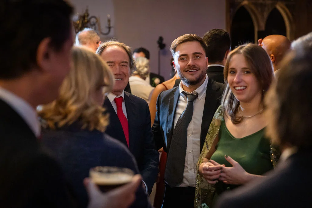 Happy wedding guests chatting and smiling together during a lively drinks reception indoors.