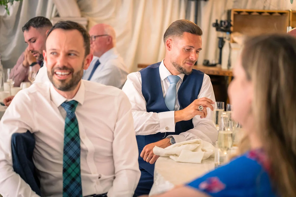 Wedding guests enjoy animated conversation and laughter during the wedding breakfast seated at tables with champagne flutes.