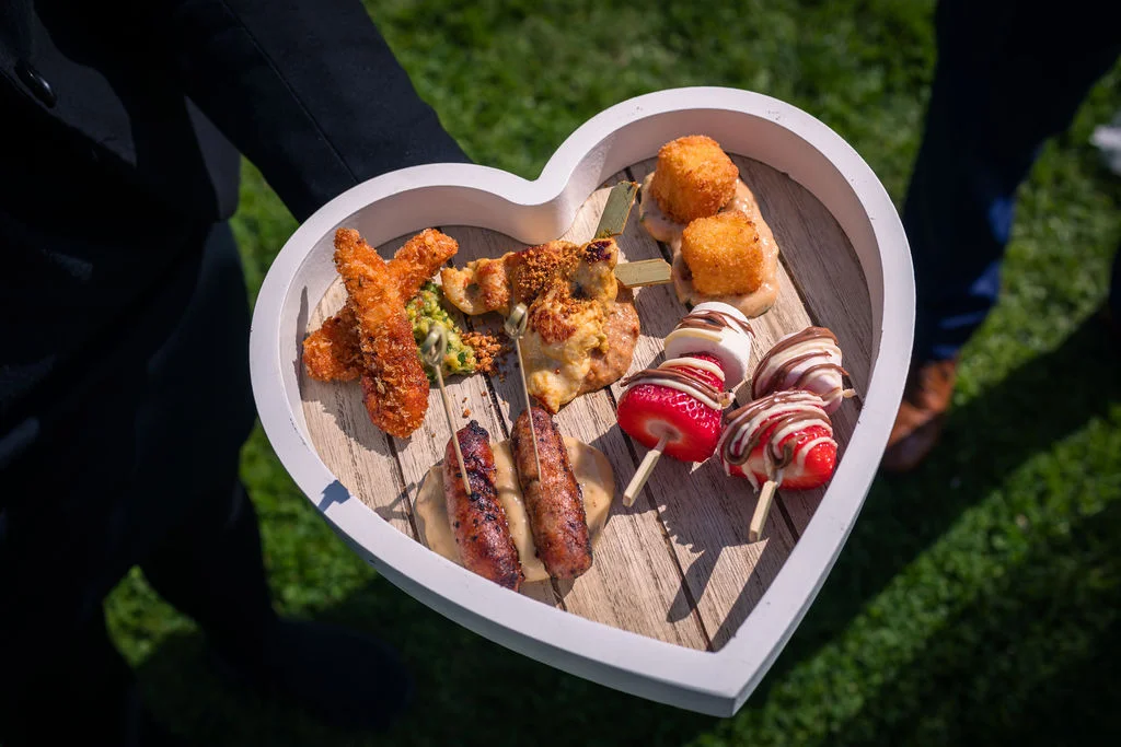 A service staff member holds a heart-shaped wooden tray filled with a variety of delicious canapés during a wedding reception.