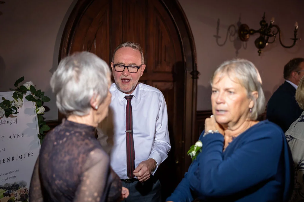 Wedding guests mingling and laughing near a wooden door and a decorative welcome sign during the evening reception.
