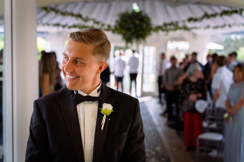 A man in a tuxedo smiles as he walks down the aisle.