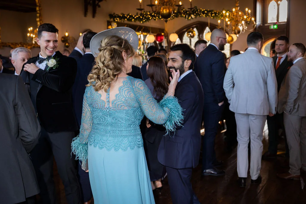 A candid photograph captures wedding guests mingling and chatting in a beautifully lit reception room adorned with festive lighting.