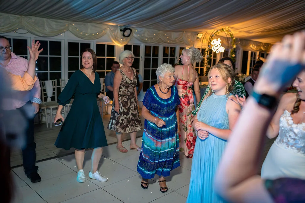 Guests enjoy dancing and laughing on a brightly lit dance floor inside a marquee wedding reception.