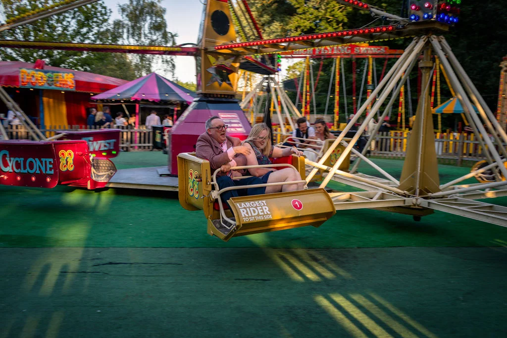 Wedding guests enjoy a funfair ride together during an evening wedding reception at an outdoor festival themed venue.