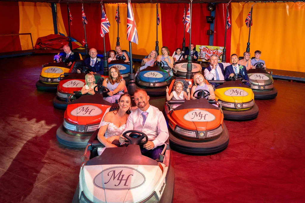 The bride and groom and their wedding guests enjoy a fun-filled ride on bumper cars inside a colourful vintage fairground tent.