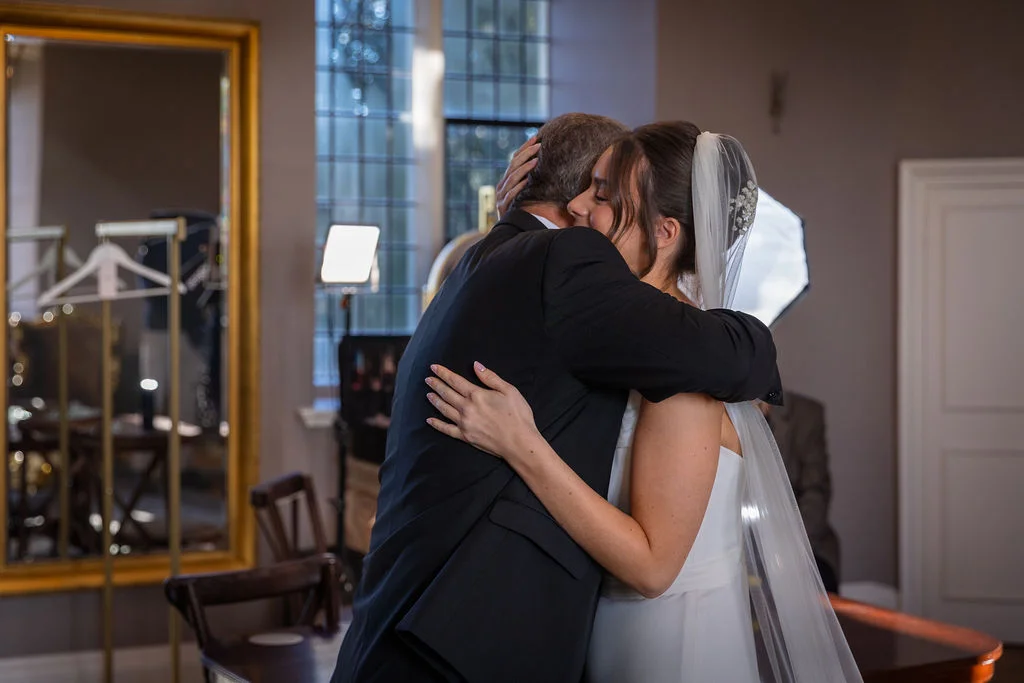 A bride shares an emotional, tender embrace and first look with her father in a light-filled room while getting ready on her wedding day.