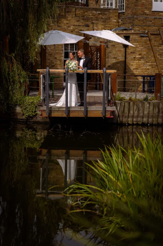 A bride and groom standing on a bridge over a pond.
