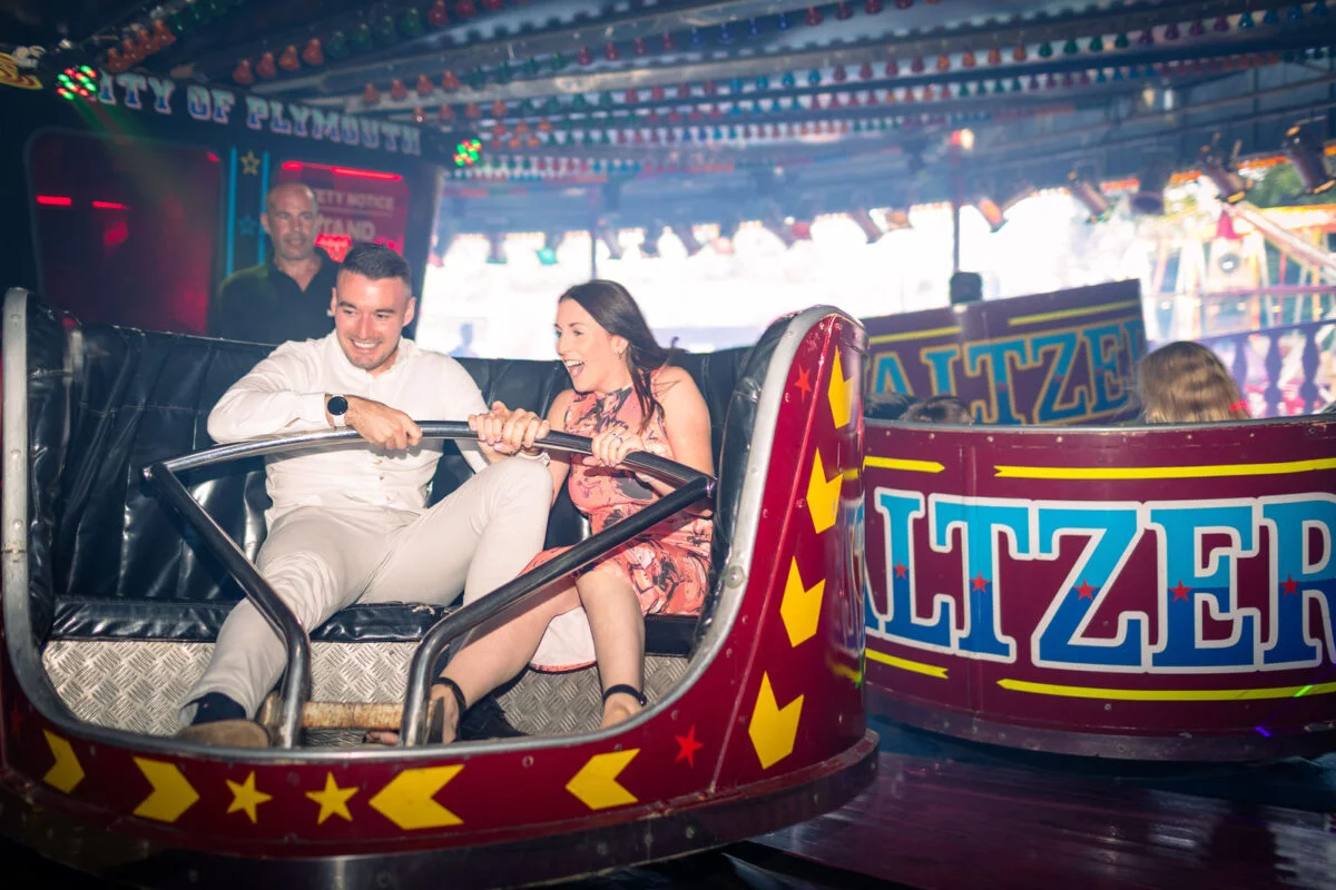 A newlywed couple laugh excitedly while riding a Waltzer fairground ride together during their evening wedding reception celebrations.