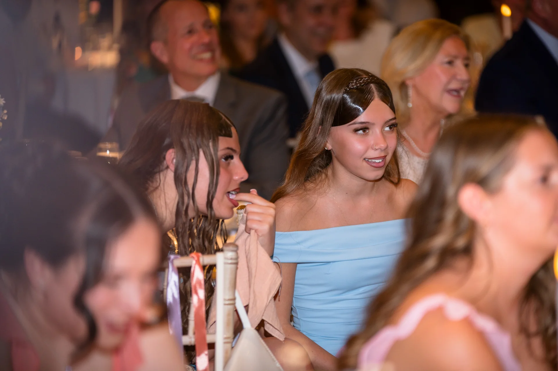 Guests are seated and laughing during the wedding breakfast speeches, with one smiling young woman wearing an off-the-shoulder blue dress.