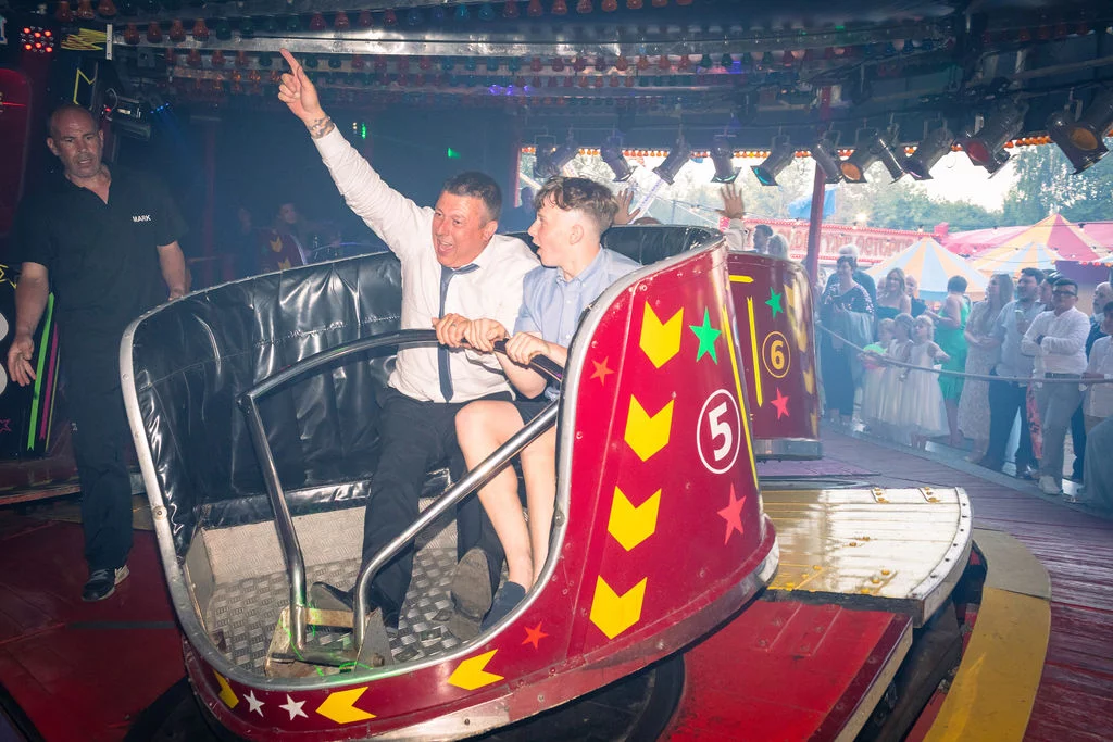 Wedding guests enjoy a thrilling ride on a fairground attraction during an evening festival-style reception celebration.