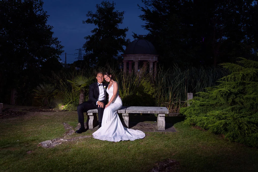 A bride and groom sitting on a bench at night.