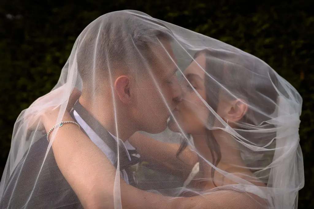 A bride and groom kissing under a veil.