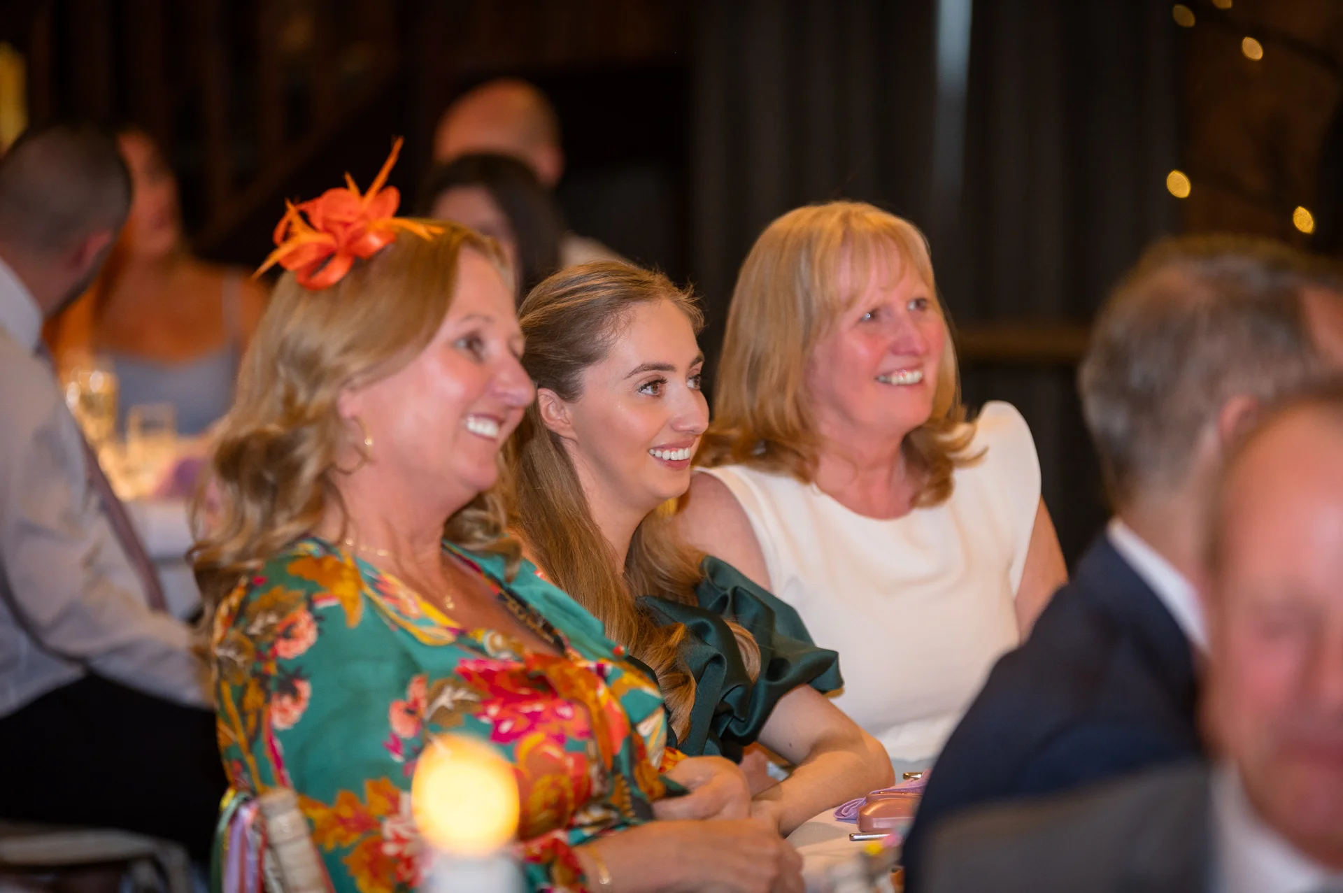 Wedding guests laugh joyfully while listening to speeches during the reception.